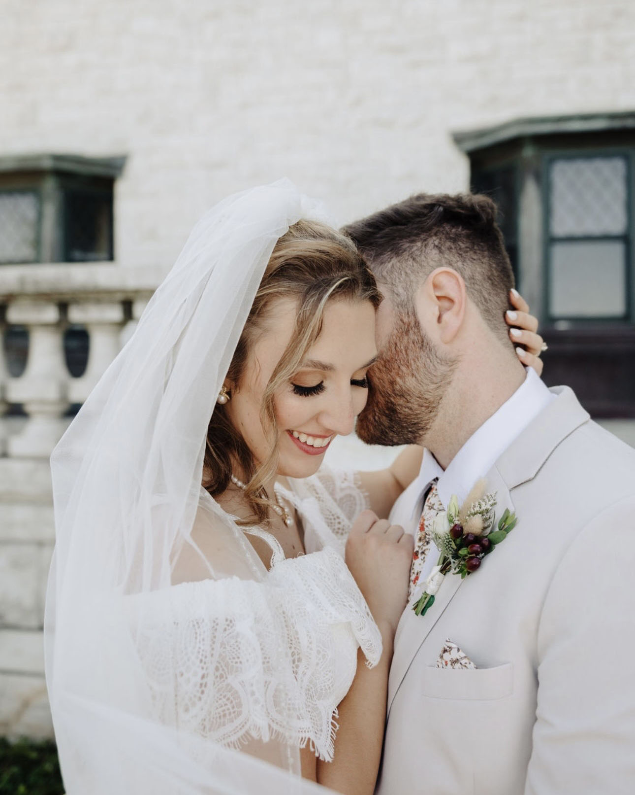 A close-up, romantic shot of a bride and groom leaning in together, featuring a lace wedding dress and a groom’s floral tie.